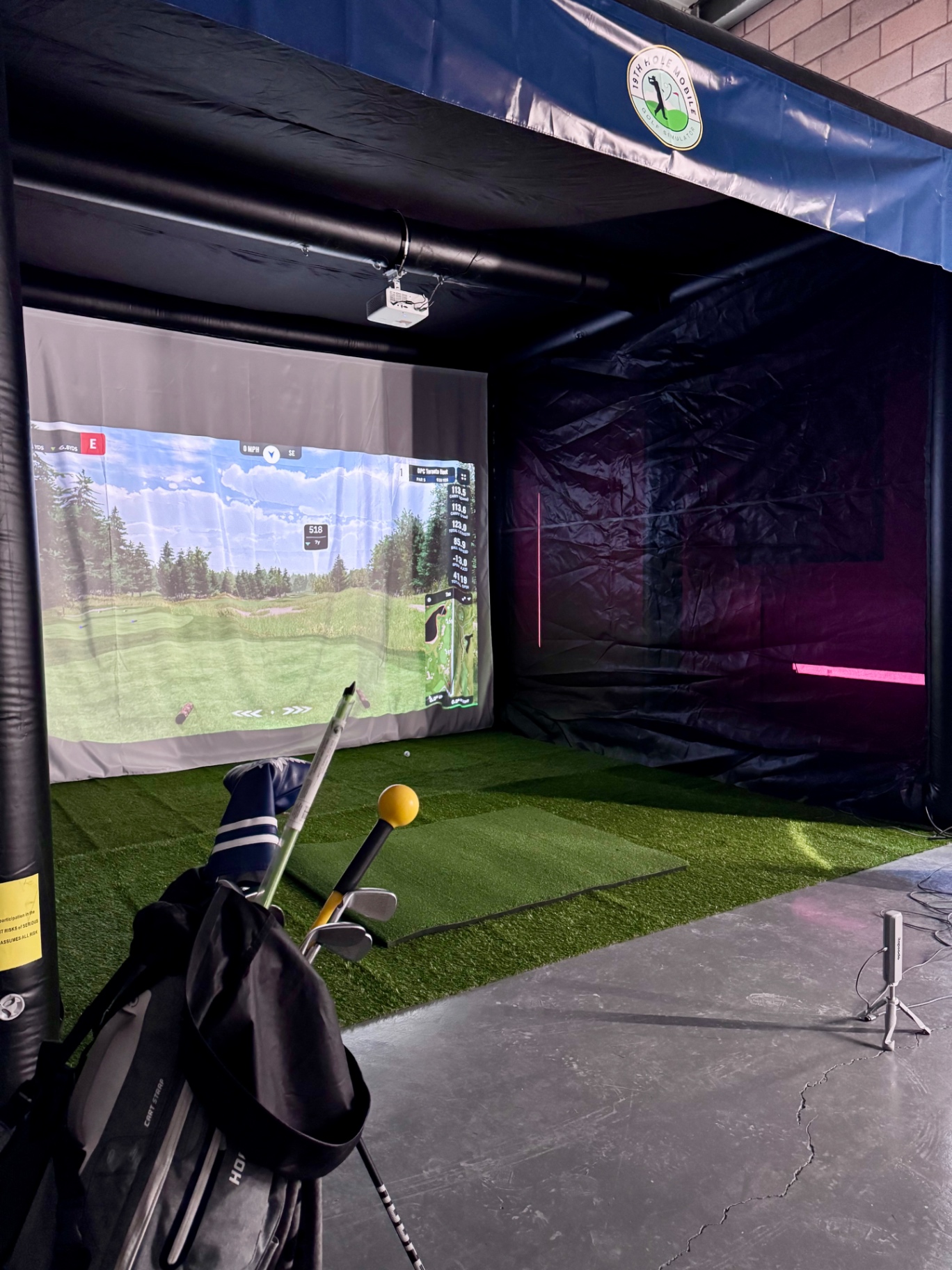 Simulator screen showing live shot data inside a venue with clubs staged nearby